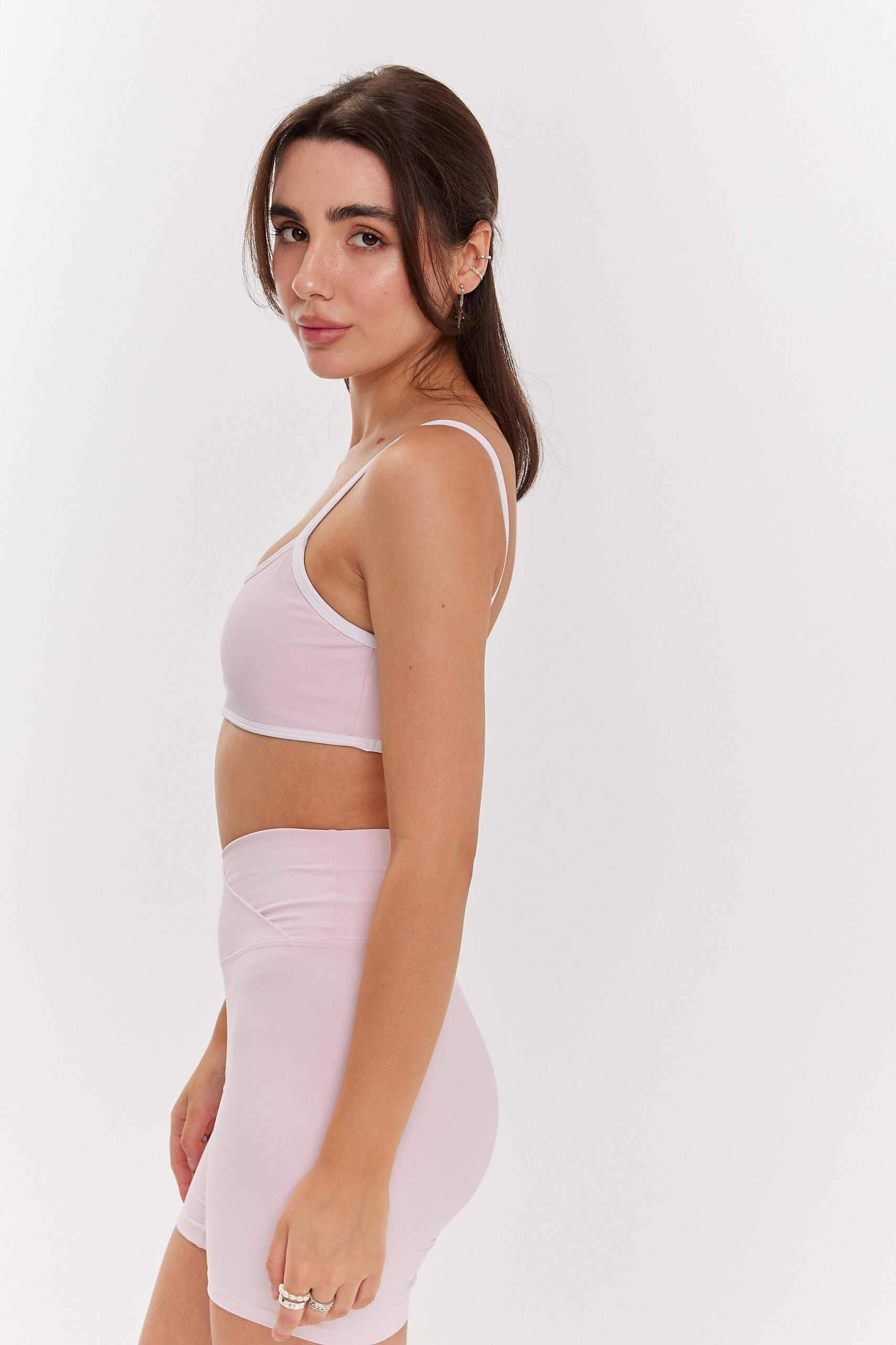 Zdjęcie kobiety bokiem różowych spodenek z zakładką i rózowego stanika z białymi ramiączkami