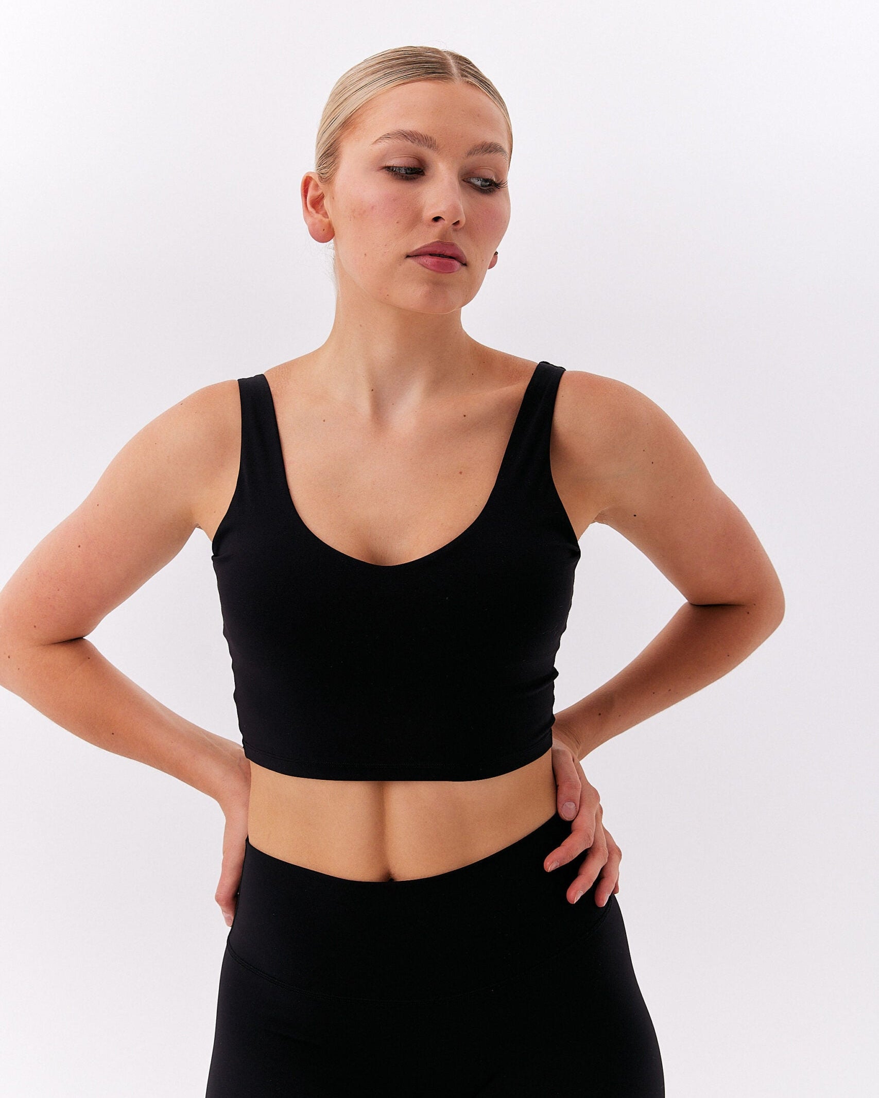 Kobieta z rękami na biodrach w czarnym krótkim topie na grubych ramiączkach