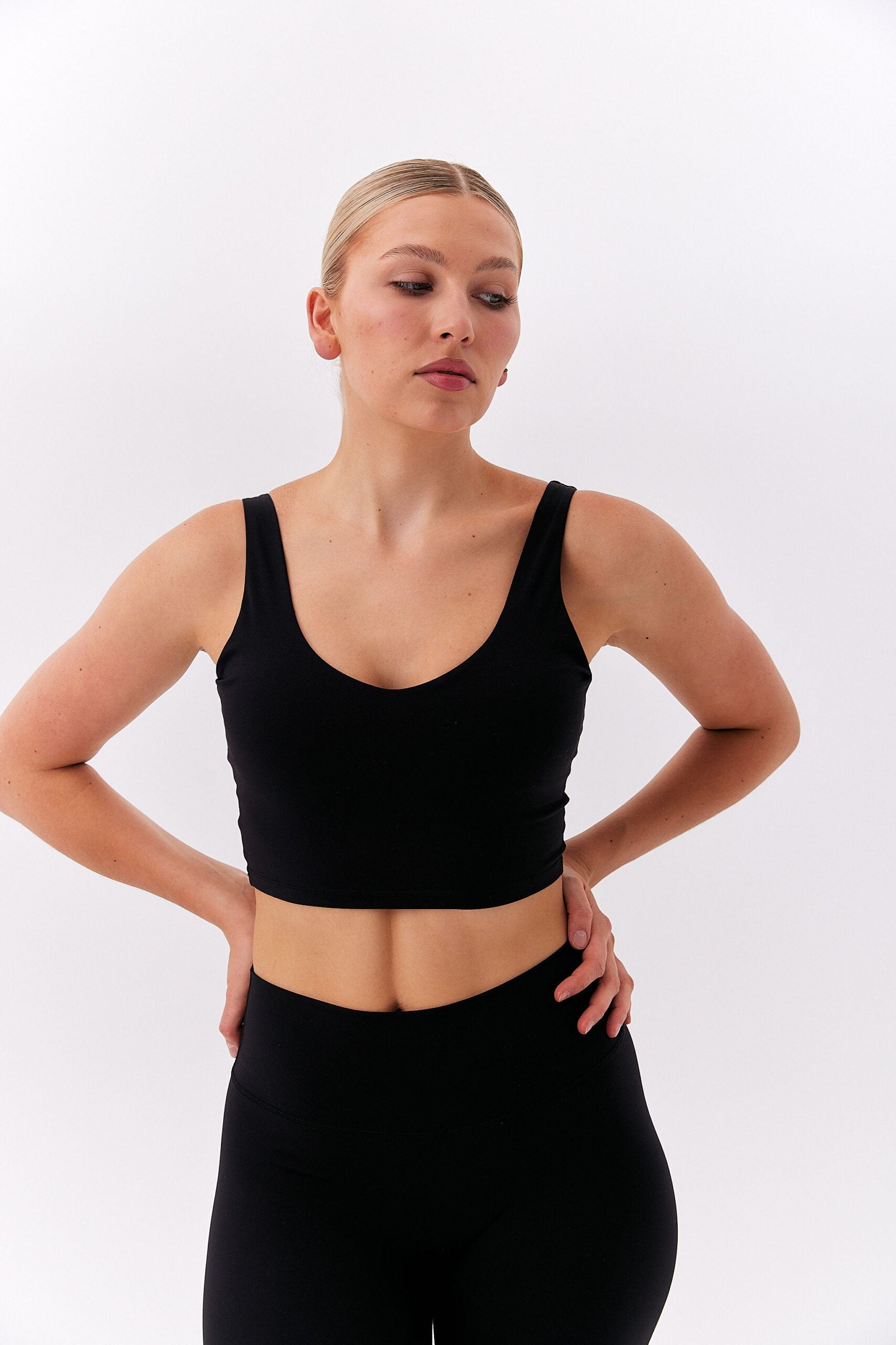 Kobieta z rękami na biodrach w czarnym krótkim topie na grubych ramiączkach